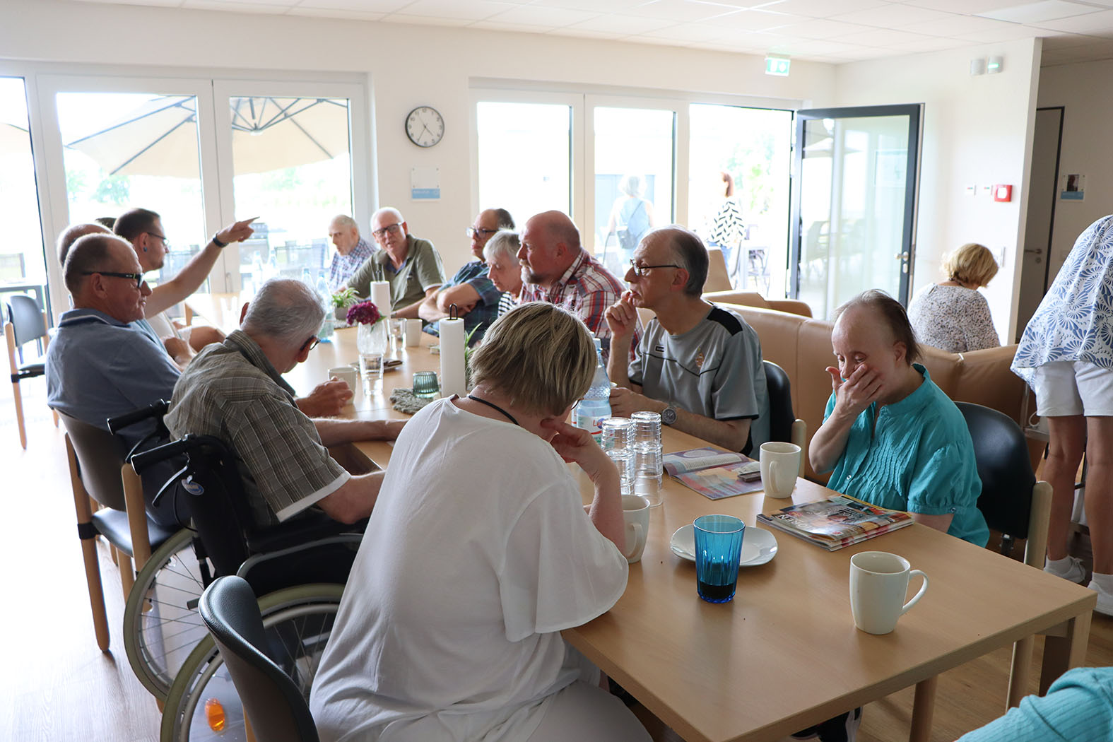 Eine Gruppe von Menschen sitzt an Tischen und unterhält sich. Es sind viele Männer und Frauen zu sehen.