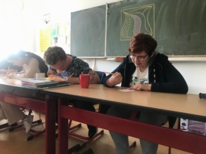Eine Person sitzt an einem Schreibtisch und schreibt. Es gibt Bücher und einen Becher auf dem Tisch.