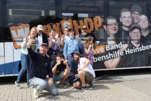 Eine Gruppe von Menschen sitzt und steht vor einem Gebäude. Sie lächeln und schauen in die Kamera.