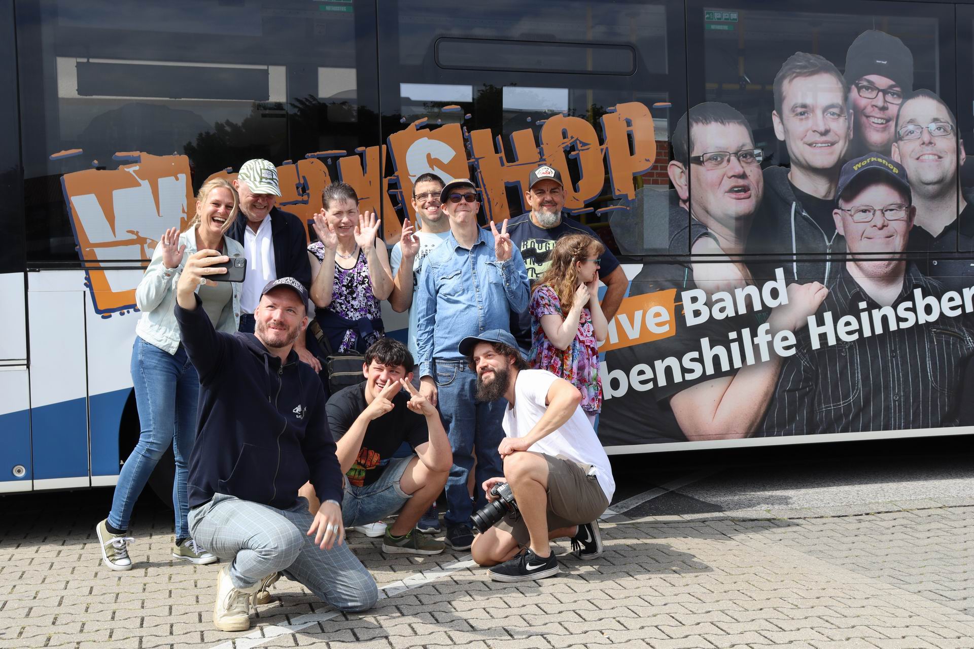 Eine Gruppe von Menschen sitzt und steht vor einem Gebäude. Sie lächeln und schauen in die Kamera.