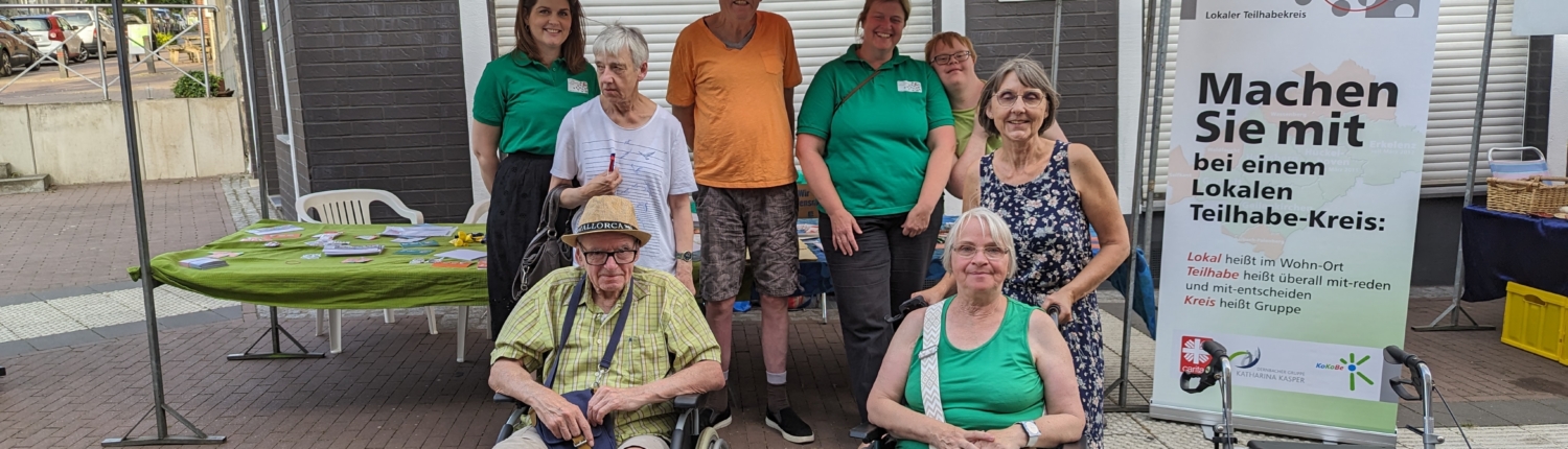 Gruppe von Menschen in Rollstühlen und Stehenden vor einem Informationsstand, der auf Barrierefreiheit und Inklusion hinweist.
