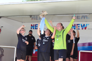 Mannschaftsfeier nach dem Sieg, Spielerinnen jubeln auf der Bühne und halten den Pokal hoch, mit Medaillen um den Hals und strahlenden Gesichtern.