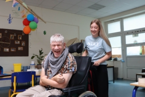 Ein Mann sitzt im Rollstuhl und lacht. Eine Frau steht daneben und lächelt.