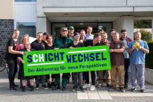 Eine Gruppe von Menschen steht vor einem Gebäude. Sie lächeln und schauen in die Kamera.
