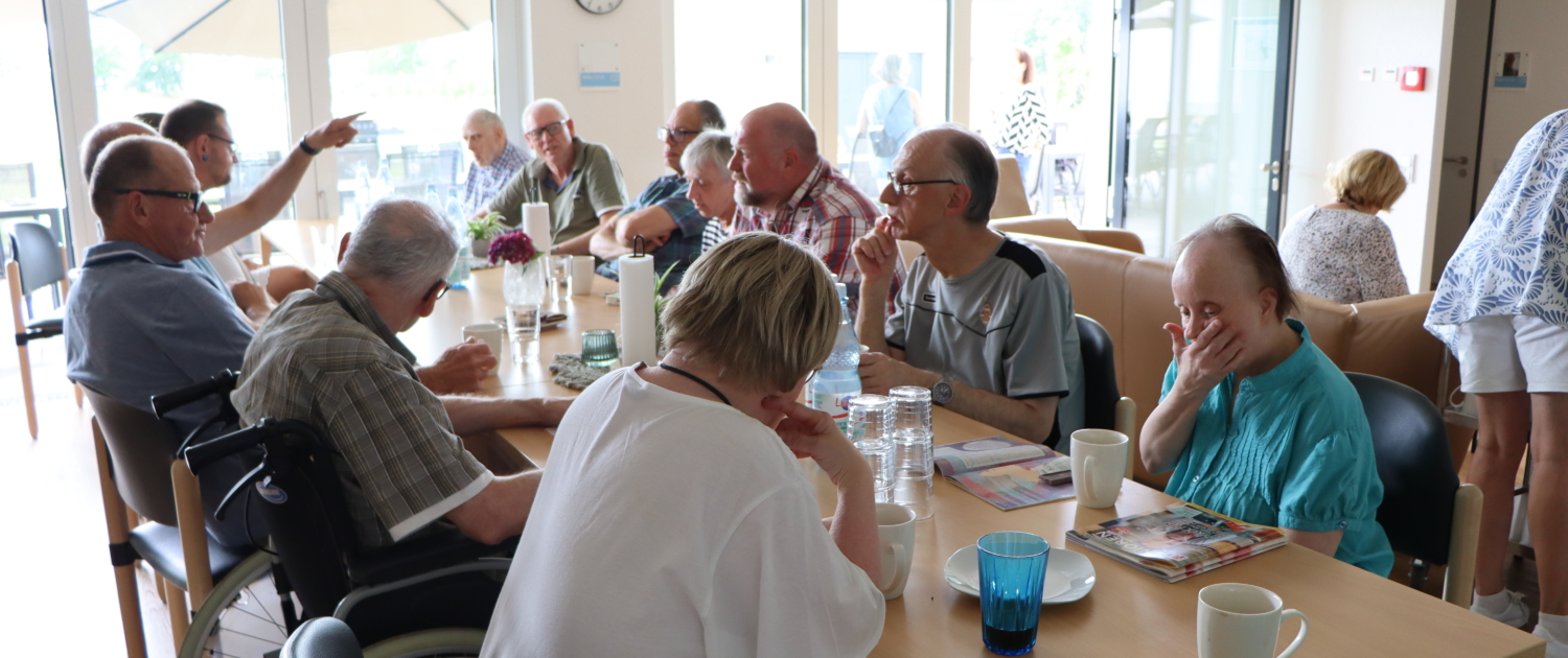 Eine Gruppe älterer Menschen sitzt an einem Tisch. Sie unterhalten sich und trinken etwas.