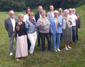 Eine Gruppe von Menschen steht auf einer Wiese. Sie lächeln und schauen in die Kamera.
