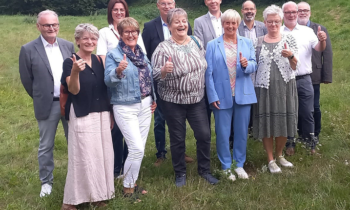 Eine Gruppe von Menschen steht auf einer Wiese. Sie lächeln und schauen in die Kamera.