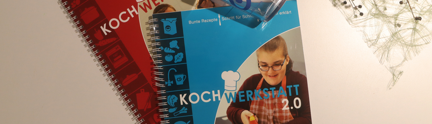 Zwei Broschüren in rot und blau liegen auf einem Tisch, die Informationen zu einem bestimmten Thema bieten. Die blaue Broschüre zeigt eine Person, die mit Lebensmitteln arbeitet, während die rote Broschüre eine andere Person abbildet.