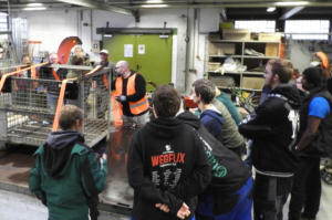 Arbeiter stehen in einer Lagerhalle. Ein Mann trägt eine Warnweste. Es gibt viele Kisten und Kartons im Hintergrund.