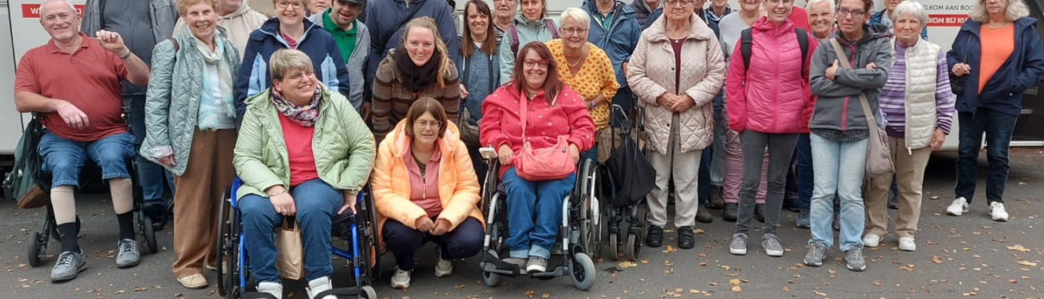 Gruppe von Menschen unterschiedlichen Alters, darunter Senioren in Rollstühlen und Stehenden, die gemeinsam im Freien posieren. Sie tragen bunte Kleidung und lächeln, was eine freundliche Gemeinschaftsatmosphäre vermittelt.