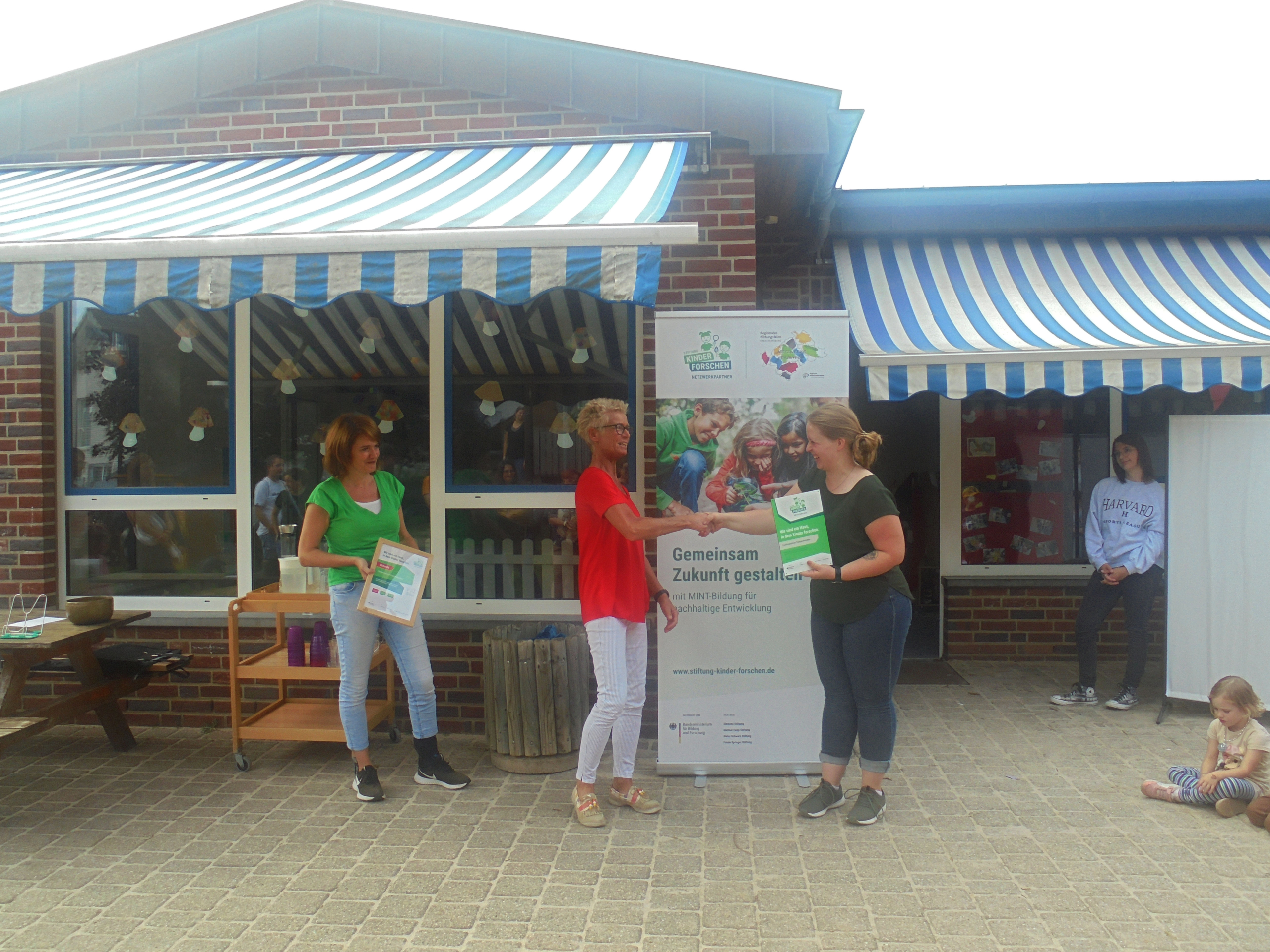 Menschen stehen unter einem Vordach. Einige halten Flyer in der Hand.