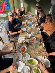 Eine Gruppe von Personen sitzt an einem Tisch im Freien und genießt ein reichhaltiges Essen mit verschiedenen Gerichten und Getränken.