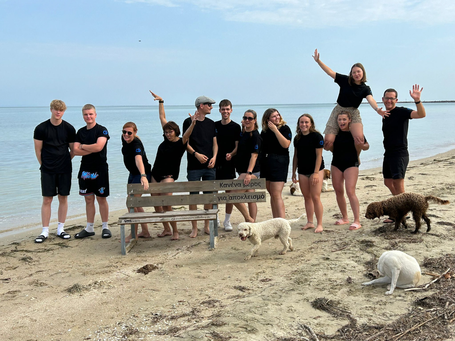 Eine Gruppe von Jugendlichen steht auf einem Strand. Ein Hund steht neben ihnen.