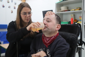 Ein Mann trinkt aus einer Tasse. Eine Frau hält ihm die Tasse hin.