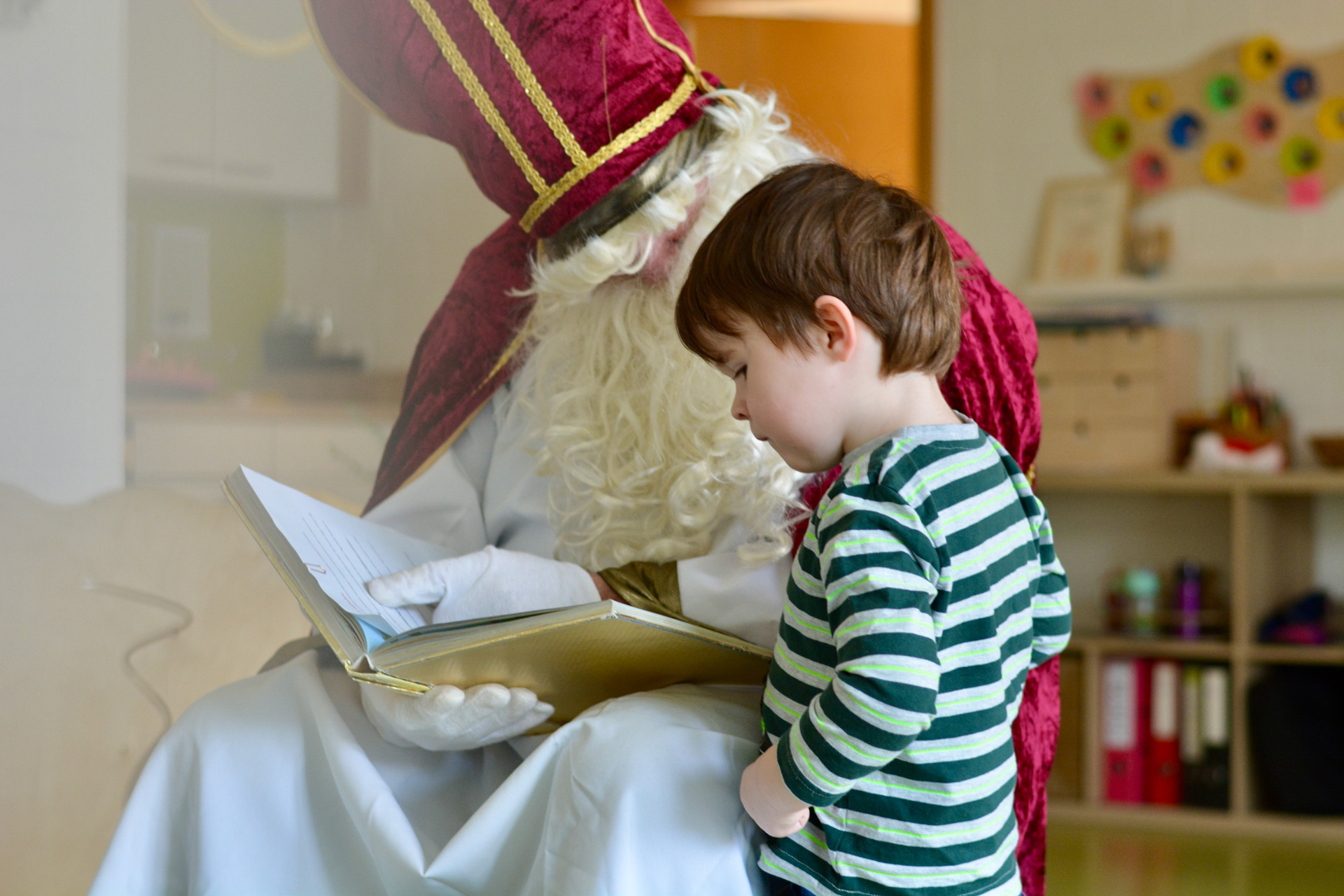Kind hört aufmerksam dem Weihnachtsmann zu, während er in einem Buch liest. Festliche Atmosphäre mit Weihnachtsdekor.