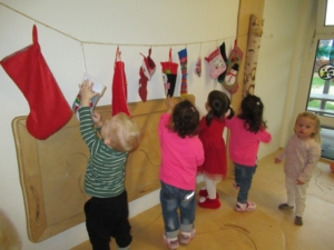 Kinder hängen kreative Bastelarbeiten an einer Schnur auf, während sie in einem hellen Raum spielen. Die farbenfrohen Kunstwerke zeigen verschiedene Designs und Farben.