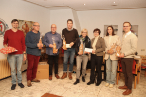 Eine Gruppe von Menschen steht in einem Raum. Einige halten Päckchen oder Umschläge in der Hand.