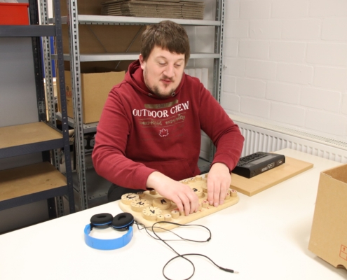 2023-12-15_Mike Musikgruppe (51) Ein Mann schneidet mit einem Messer etwas aus. Er trägt ein rotes T-Shirt. Hinter ihm stehen Kartons.