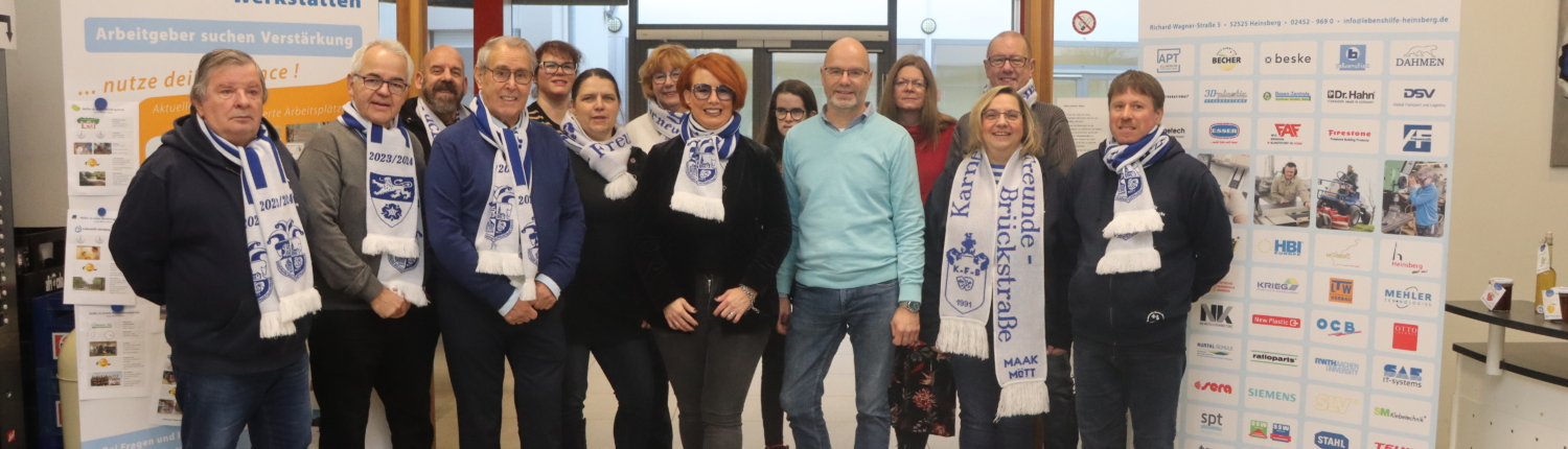 Eine Gruppe von Menschen steht vor einem Gebäude. Sie lächeln und schauen in die Kamera.