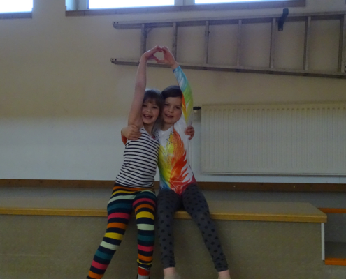 Zwei Kinder sitzen auf einer Bank und umarmen sich. Sie lächeln.