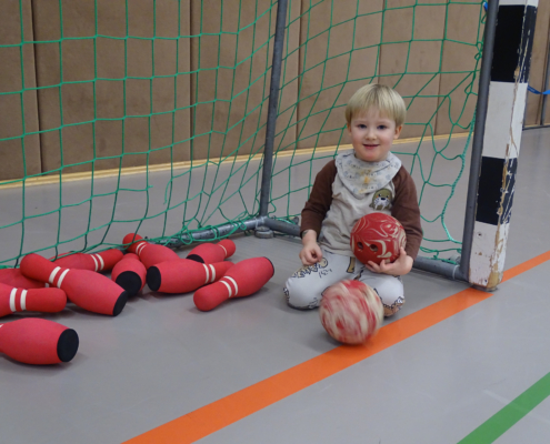 Ein Kind sitzt auf dem Boden und hält zwei Bälle. Hinter dem Kind sind noch mehr Bälle zu sehen.