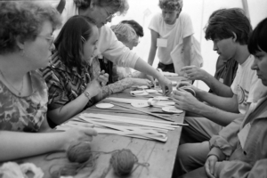 Eine Gruppe von Menschen, die an einem Tisch sitzen und gemeinsam kreative Bastelarbeiten durchführen. Die Szene zeigt verschiedene Materialien und Werkzeuge, während die Teilnehmer konzentriert arbeiten.