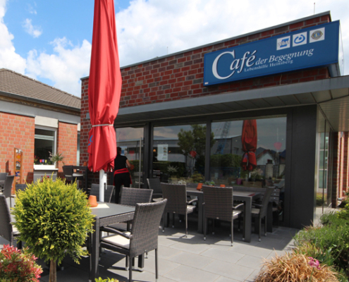 Außenansicht eines Cafés mit roten Sonnenschirmen, gemütlichen Sitzplätzen und einer einladenden Atmosphäre. Ideal für entspannte Kaffeepausen und geselliges Beisammensein.