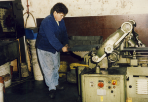 Ein Mann arbeitet an einer Maschinenwerkstatt, während er eine Werkzeugmaschine bedient. Im Hintergrund sind verschiedene Maschinen und Werkzeuge zu sehen, die für die Metallbearbeitung verwendet werden.