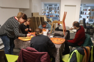 Gruppe von Menschen, die an einem kreativen Workshop teilnehmen und verschiedene Kunstprojekte mit Holzmaterialien bearbeiten.