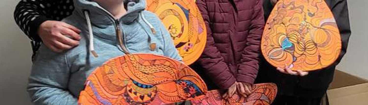 Gruppe von fünf Personen, die stolz bemalte Stühle mit bunten, kreativen Designs präsentieren, in einem hellen Raum mit grauem Boden.