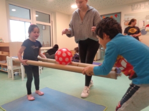 Kinder spielen mit einem Stab und einem Ball. Ein Kind steht auf einer blauen Matte.