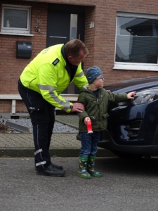 Ein Polizist gibt einem Kind einen Stift. Das Kind trägt Regenboots.