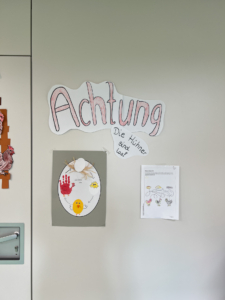 Bunte Wandgestaltung mit dem Wort "Achtung" und einem dekorierten Ei sowie einem Informationsblatt. Ideal für ein kreatives Umfeld oder eine Kindereinrichtung.