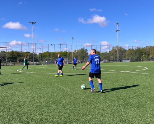 Fußballspieler stehen auf einem grünen Platz. Sie schauen einen Ball an. Es ist ein sonniger Tag.