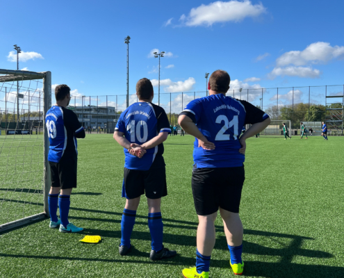 Drei Jungen stehen auf einem Fußballplatz. Sie tragen Fußballtrikots.