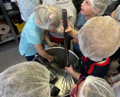 2024-05-16_Besuch Küche 1 (21)-2 Personen mit Hauben stehen in einer Küche. Sie schauen auf eine Schüssel.