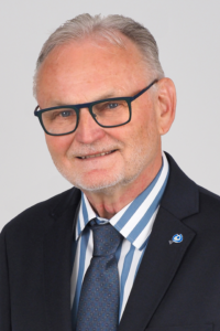 Ein freundlich lächelnder Mann mit Brille und Anzug.