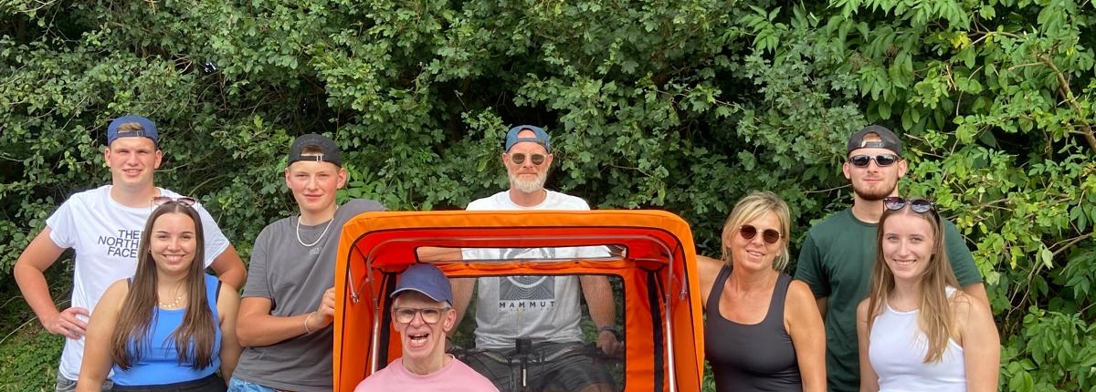 Eine Gruppe von Menschen und ein Hund stehen vor einem offenen Jeep. Es ist ein sonniger Tag.