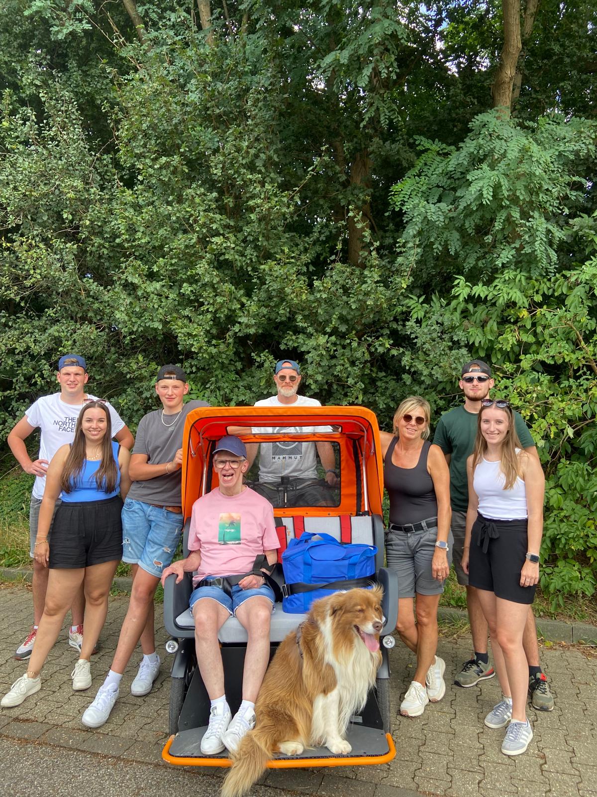 Eine Gruppe von Menschen und ein Hund stehen vor einem offenen Jeep. Es ist ein sonniger Tag.