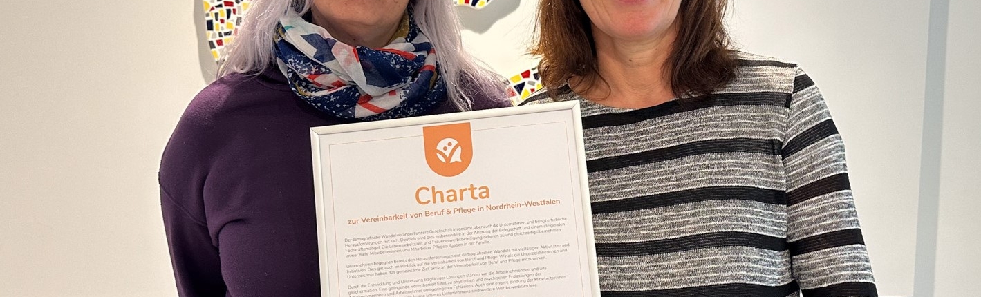 Eine Frau hält ein Papier in der Hand. Sie trägt eine schwarze Jacke und eine bunte Krawatte.