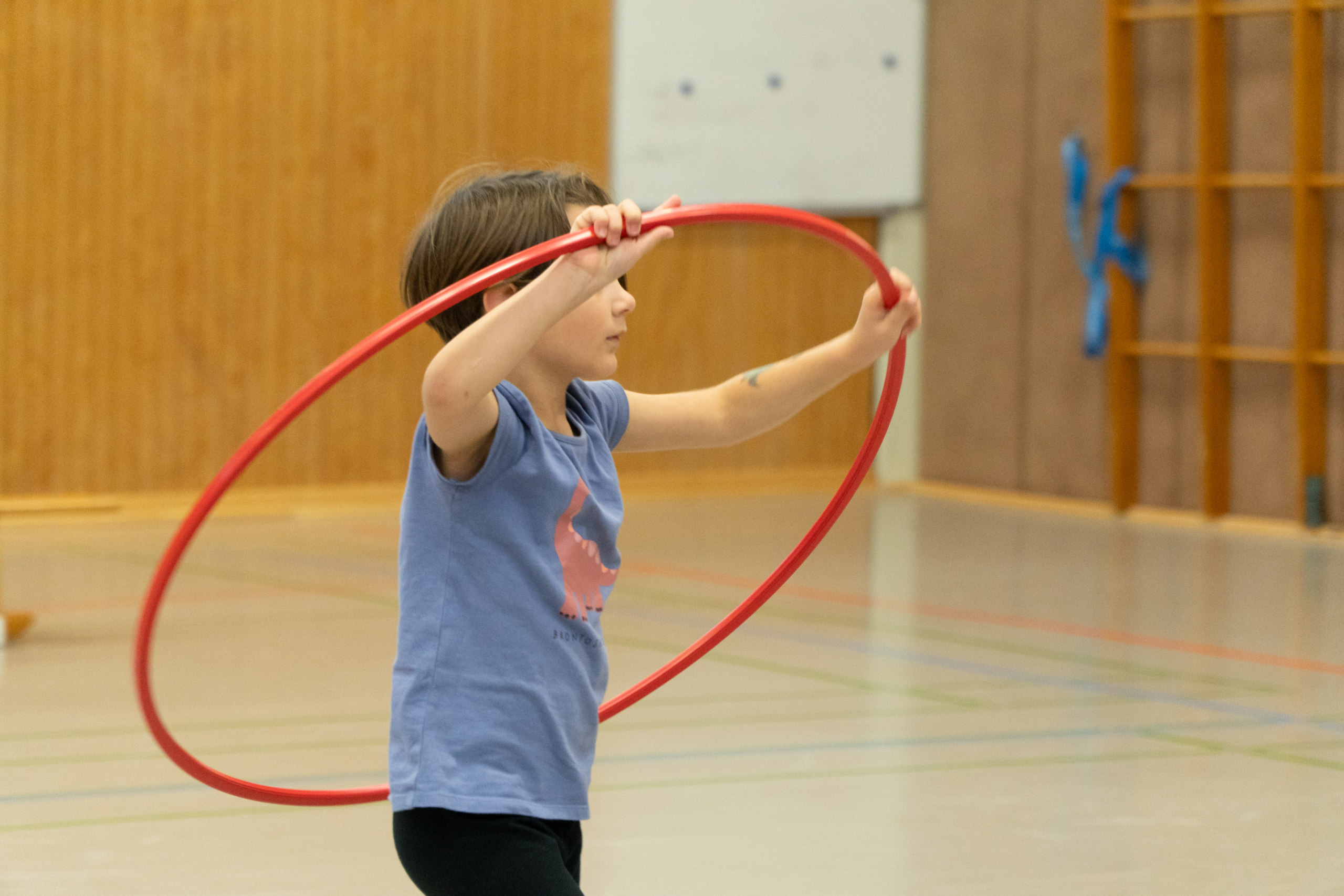 Ein Kind übt mit einem Hula-Hoop-Reifen in einer Turnhalle, fördert Bewegung und Koordination.