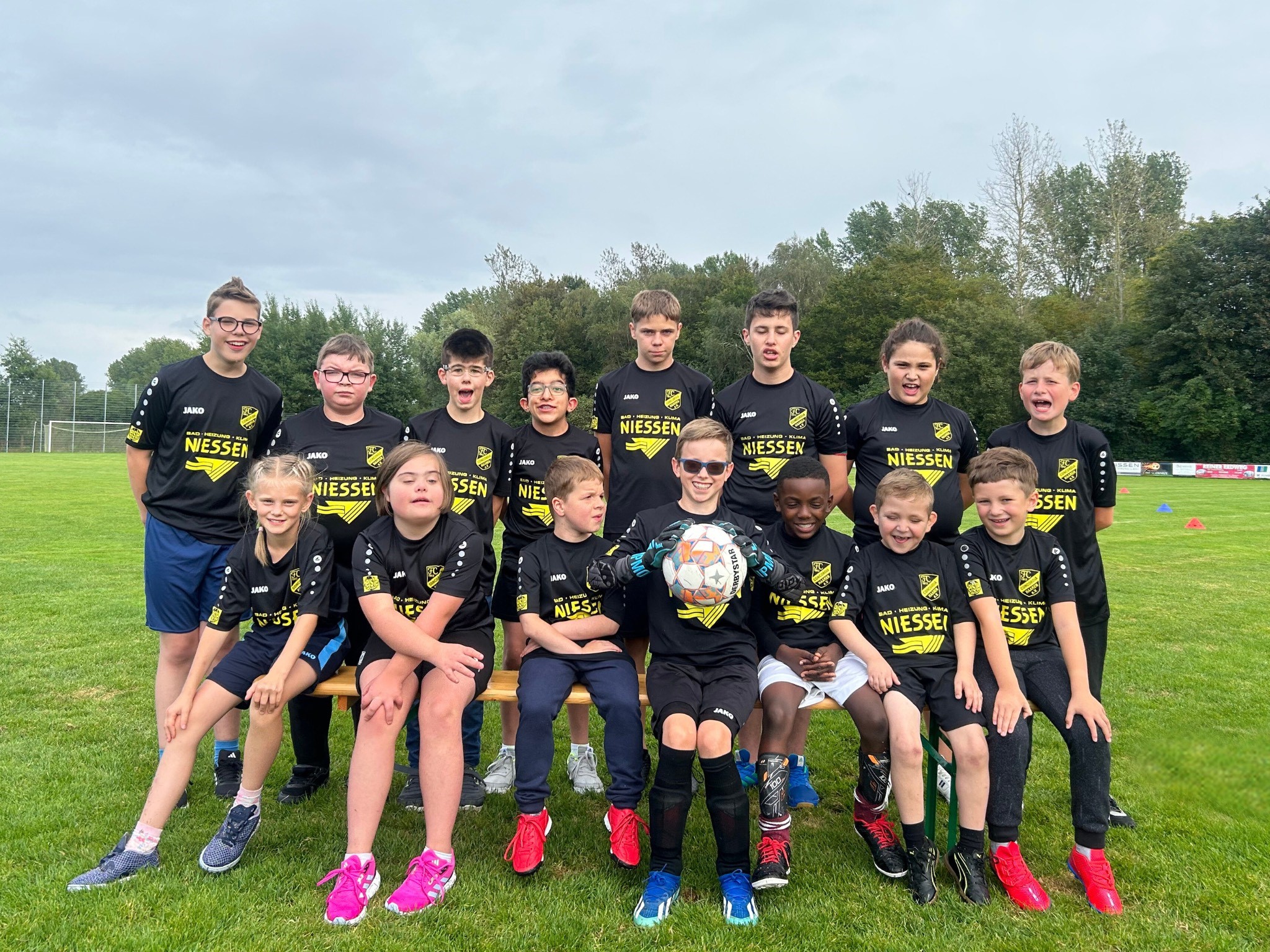Gruppenfoto einer Jugendfußballmannschaft in schwarzen Trikots, die auf einem Rasenplatz posiert. Die Spieler sind zwischen 8 und 12 Jahren alt und lächeln freundlich in die Kamera.