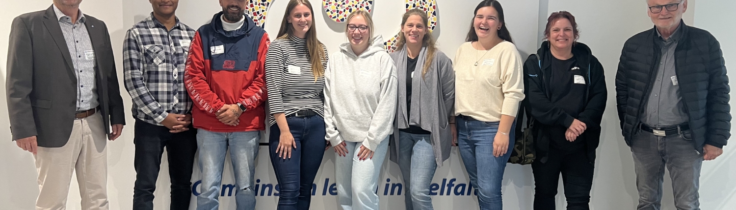 Eine Gruppe von Personen steht vor einer Wand mit vielen Farben. Es sind verschiedene Menschen dabei.