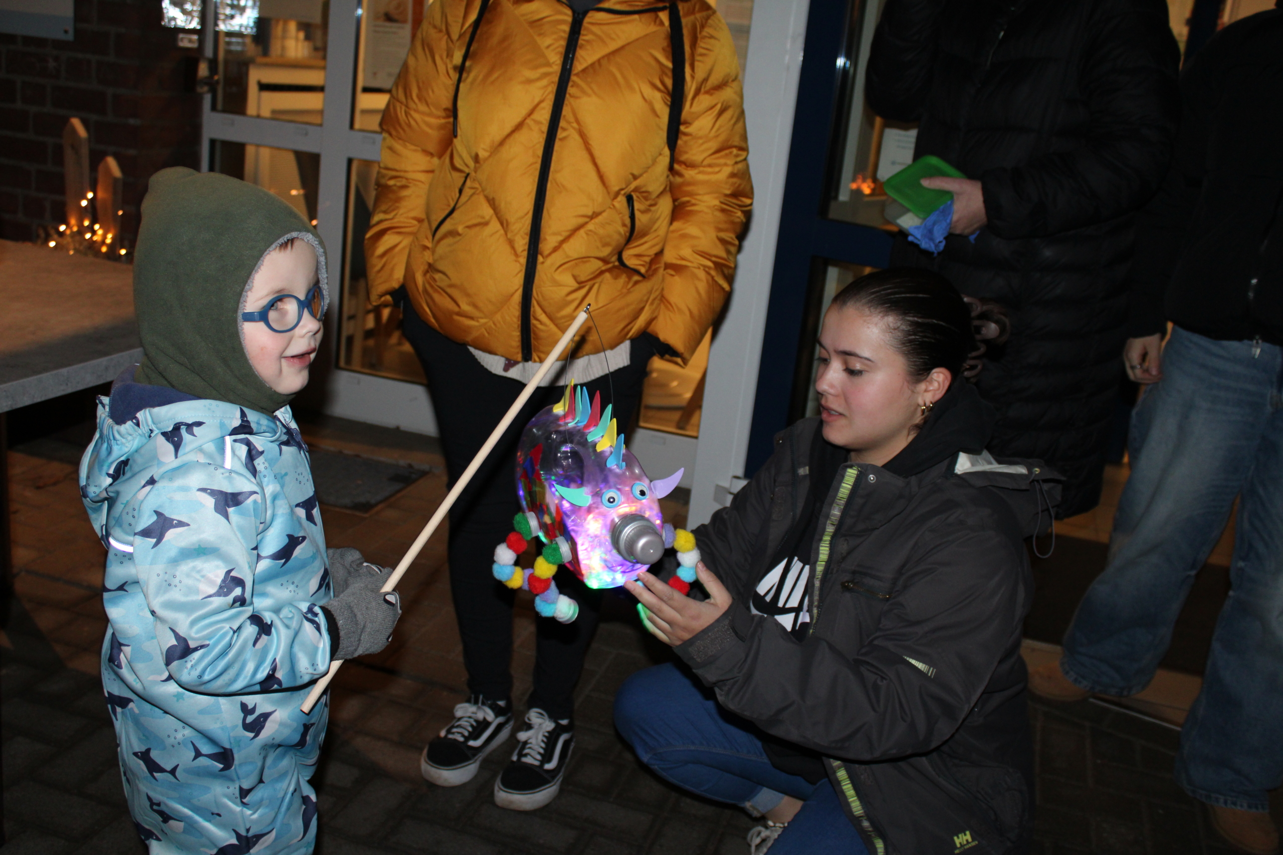 Ein Kind hält eine leuchtende Figur. Eine Frau sitzt daneben und schaut. Es ist dunkel draußen.