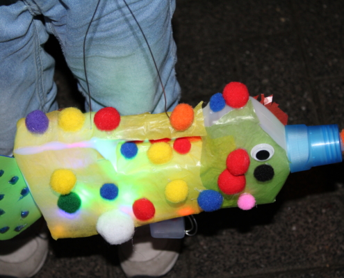 Bunte selbstgemachte Wasserpistole mit Pompons und Lichtern, gehalten von einem Kind.