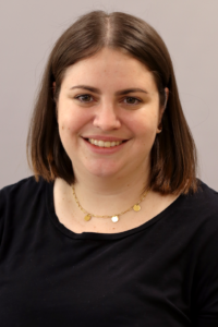 Eine Frau lächelt in die Kamera. Sie hat kurze, braune Haare und trägt eine schwarze Bluse.