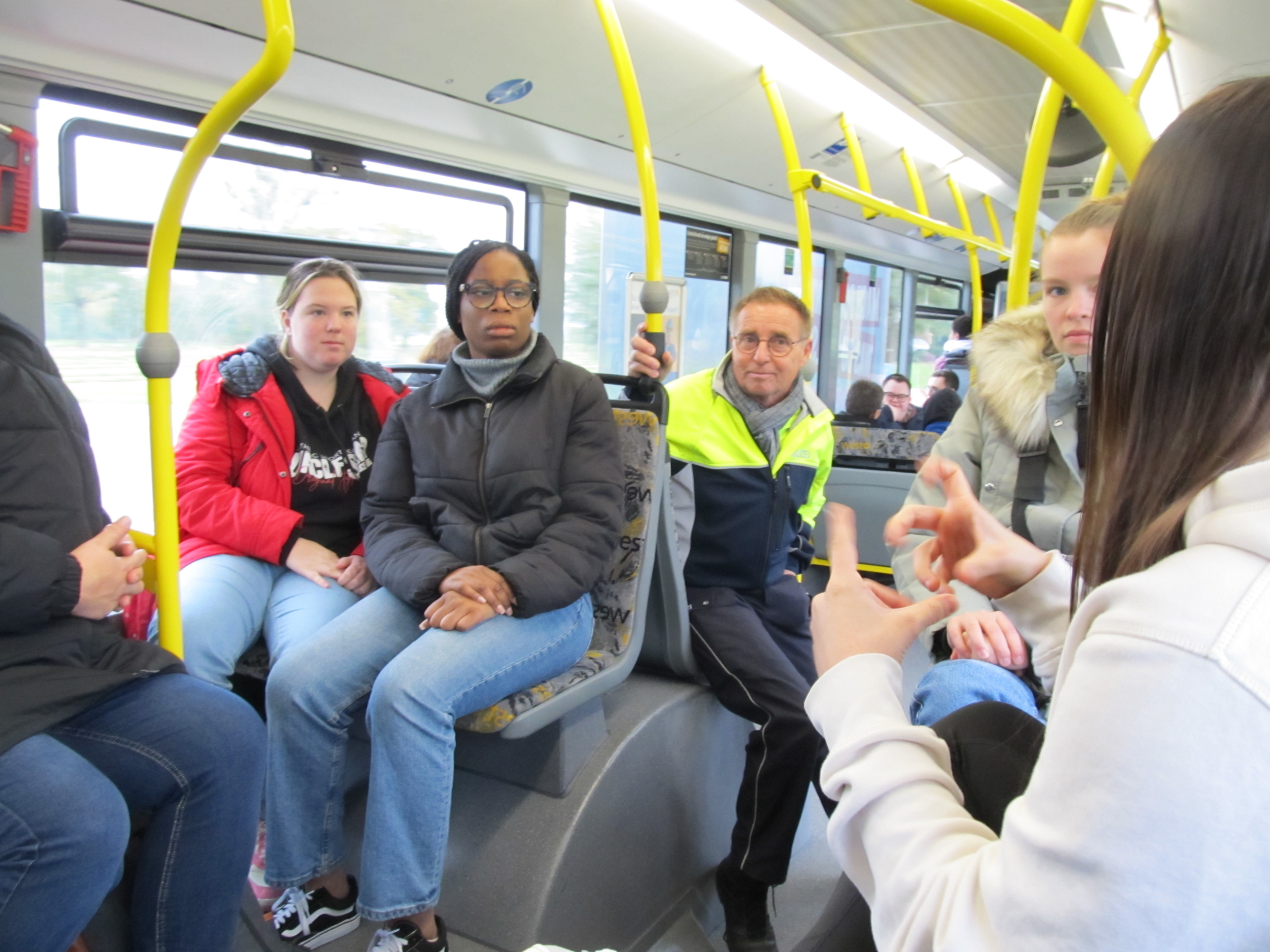 Menschen sitzen in einem Bus. Einige schauen nach vorne, andere reden miteinander.