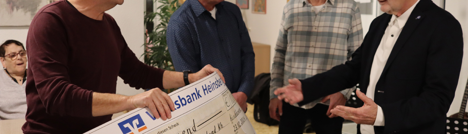 Personen übergeben einen großen Scheck in einem modernen Büro. Die Szene zeigt eine feierliche Übergabe, bei der vier Männer miteinander interagieren.
