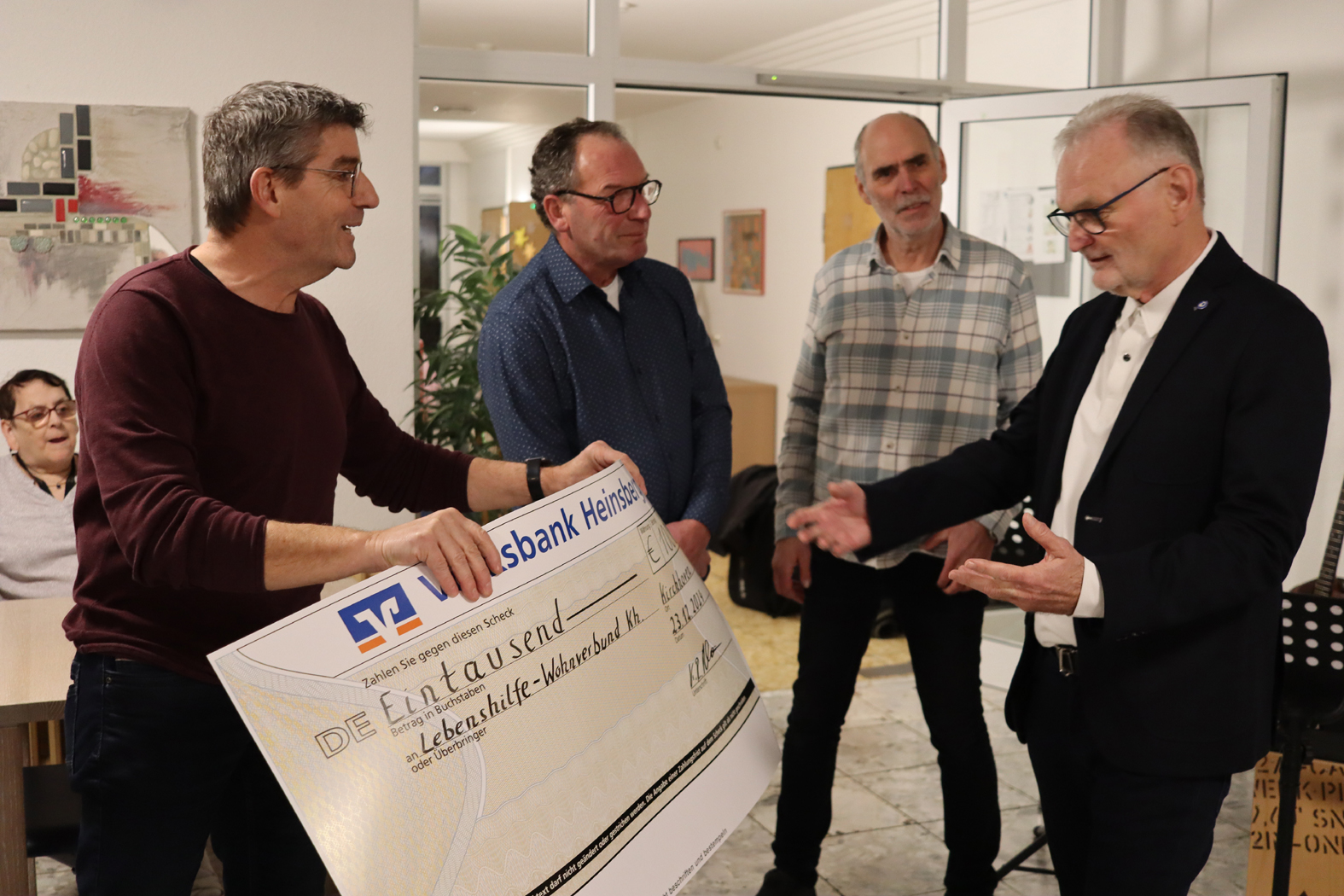Personen übergeben einen großen Scheck in einem modernen Büro. Die Szene zeigt eine feierliche Übergabe, bei der vier Männer miteinander interagieren.