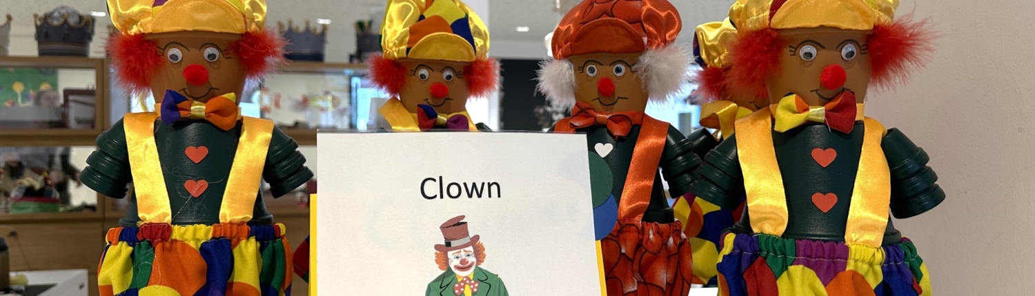 Bunte Clowns stehen auf einem Tisch. Sie haben rote Nasen und lustige Hüte.